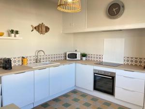 La cuisine est équipée de placards blancs, d'un évier et d'un four micro-ondes. dans l'établissement Joli appartement avec vue mer, à Narbonne