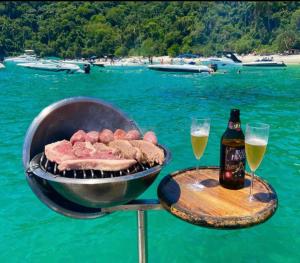 een barbecue met vlees en twee glazen bier bij Passeios de lancha em Angra dos Reis in Angra dos Reis