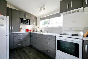 a kitchen with gray cabinets and white appliances at Opunake Break - Opunake Holiday Home in Opunake