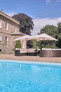 a swimming pool with two umbrellas and a building at The Manor Holcombe Luxury House Pool & Hot-tub in Holcombe
