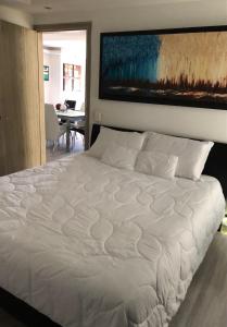 1 dormitorio con 1 cama blanca y una pintura en la pared en Habitacion Cama Queen, en Bogotá