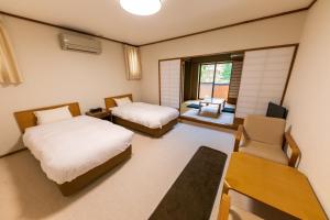 a room with two beds and a table and a chair at Hakone Sengokuhara Toranoyu in Hakone
