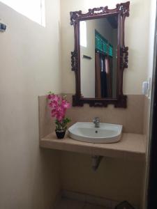 a bathroom sink with a mirror and a vase with flowers at Damuh Guest House in Ubud