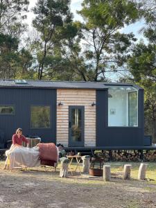 une femme assise devant une petite maison dans l'établissement Wild Life Cabin 1 - Grampians, à Halls Gap