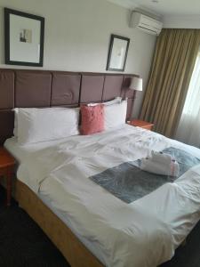 uma cama grande com lençóis brancos e almofadas vermelhas em Protea Hotel by Marriott Harrismith Montrose em Harrismith