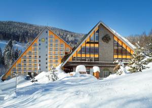 a large building with snow in front of it at Pinia Hotel & Resort in Špindlerův Mlýn