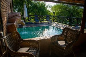 a swimming pool with two chairs and a waterfall at Adventure Bush House in Marloth Park