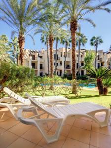 - deux chaises longues blanches sur une terrasse avec des palmiers dans l'établissement Roda Golf Resort - 9309, à San Javier