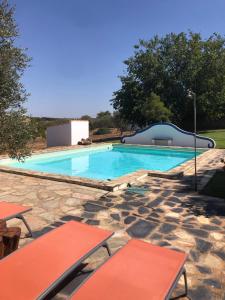 a swimming pool with red tables and a stone patio at Vale de Camelos Country House, Alentejo, Portugal. in Alcaria Ruiva