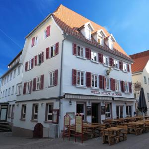 a white building with red shuttered windows and wooden tables at Hotel Goldener Hirsch Mosbach in Mosbach
