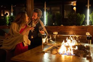 Ein Mann und eine Frau trinken Wein vor einem Feuer. in der Unterkunft Hotel Nordik in Andalo