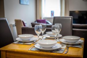 a wooden table with plates and wine glasses on it at Douglas House Apartments in Nairn