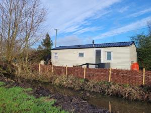 Ein weißes Haus hinter einem Zaun neben einem Fluss in der Unterkunft Bimble Lodge in Langport