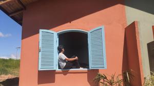 eine Person, die in einem Fenster eines Hauses sitzt in der Unterkunft Sitio Aconchego Verde Guararema in Guararema