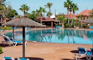 a pool at a resort with chairs and an umbrella at FUERTEVENTURAPARTMENTS in Corralejo