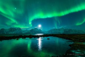 an aurora over a body of water with mountains at Lyngenfjord,Odins Hus in Olderdalen