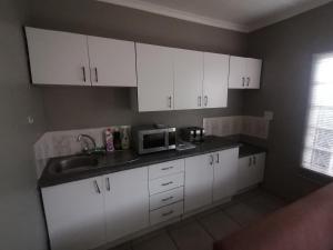 cocina con armarios blancos, fregadero y microondas en Aloe Cottage - Ramsgate Ramble Rest, en Margate