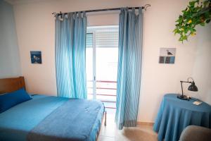 a bedroom with a bed and a window with blue curtains at Dream Holidays Cabanas in Tavira