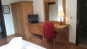 una camera da letto con scrivania, TV e sedia rossa di Albergo Bellavista a Comèlico Superiore
