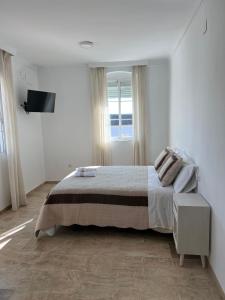 a white bedroom with a bed and a television at ATICO SUITE CLAUDIO MARCELO in Córdoba