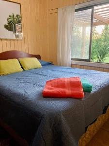 a bed with a red and green towel on it at Casa El Arrebol, sector Saltos del Laja in Cabrero