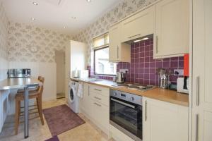 a kitchen with white cabinets and a purple tiled wall at Dairyman's Cottage in Amble