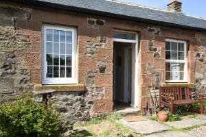 a brick house with a bench and a window at Kittiwake Cottage, Budle Bay in Bamburgh