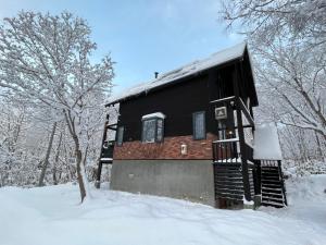 una cabaña negra en la nieve con árboles nevados en Goodfellas Onsen House en Niseko