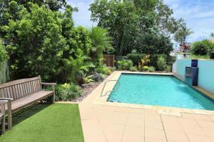 einen Pool in einem Garten mit einer Bank und Gras in der Unterkunft Coral Sands Apartment 201 in Bargara