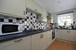 a kitchen with white cabinets and black and white tiles at East Havers in Alnwick