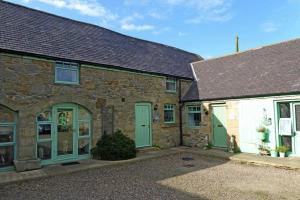 an old stone house with green doors and a dog in front at East Havers in Alnwick