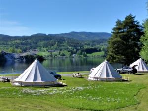 three tents on the grass next to a lake at Lystang Glamping & Cabins in Notodden