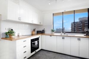 Una cocina blanca con gabinetes blancos y una ventana. en Central Getaway With Ocean Views - CoastHM, en Gold Coast
