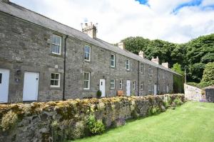 an old stone building with a stone wall and a yard at Farne View Cottage in Seahouses