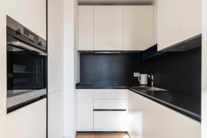 una cocina con armarios blancos y electrodomésticos negros en easyhomes-Central Tower en Milán