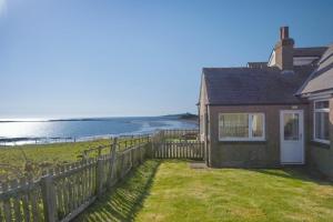 a house with a fence and a view of the ocean at Melvin Cottage in Embleton
