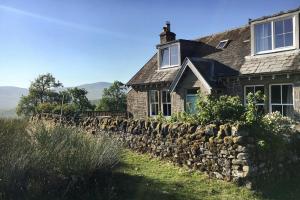 una casa de piedra con una pared de piedra delante de ella en Roughley Cottage en Newcastleton