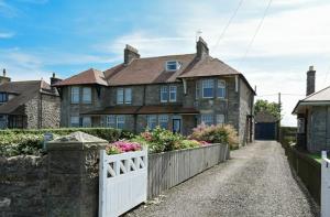 a large stone house with a white fence at Ty y Mor in Seahouses