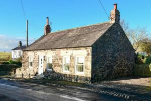 una vieja casa de piedra al lado de una carretera en West End Cottage en Embleton