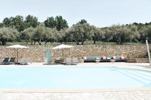 a swimming pool with chairs and umbrellas next to a stone wall at Mas la Buissonniere in Aigaliers