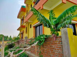 una casa amarilla con una palmera delante de ella en Tathāgata Homestay en Lumbini