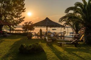 a group of tables and chairs and the ocean at sunset at Christaras Apartments in Vourvourou