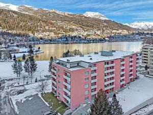 un immeuble d'appartements rose devant une étendue d'eau dans l'établissement LOGA ELEGANCE APARTMENT Skyline 1 - St. Moritz, à Saint-Moritz