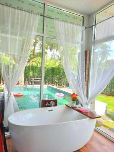 a white bath tub in a room with a large window at Amantra homestay & village in Suratthani