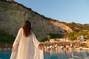 a woman in a white dress standing next to a body of water at Maya Beach Resort in Massa Lubrense