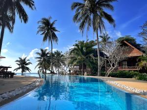a swimming pool next to a beach with palm trees at Green Papaya Beach Resort, Koh Phangan in Salad Beach