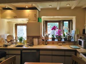 a kitchen with a counter and two windows with flowers at Bijou Cottage in Brontë Country with Wood-burning Stove & Hot Tub Spa in Haworth