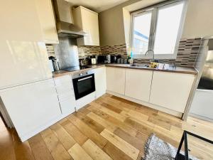 a kitchen with white cabinets and a wooden floor at Lovely two bed flat in London