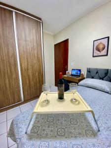 a room with a bed and two wine glasses on a table at Apto charmoso na V Planalto perto Shopping com 2 Quartos ArCond Wifi Fibra Home Office e Garagem em Dourados in Dourados