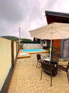un patio con sombrilla, sillas y piscina en Casa Brisa do Mar: Piscina e Conforto - Penha, en Penha
